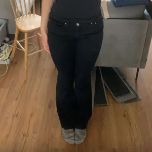 Svarta bootcut jeans med låg midja - Säljer ett par svarta jeans med bootcut-modell och låg midja från Gina tricot. Jeansen har klassisk femficksdesign, silverfärgade nitar och knapp, samt raka bakfickor. Materialet är stretchigt jeans för en bekväm passform.