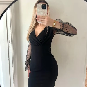 Svart kortklänning med prickiga ärmar - Supersnygg svart kortklänning med transparenta långärmade ärmar i mesh och svarta prickar. Djup v-ringning och figurnära passform. Ärmarna har volangkant vid handleden och klänningen har omlott-detalj upptill. Perfekt för dig som vill sticka ut. Aldrig använd. Säljes för att den aldrig kommer till användning. Strl står inte, men passar mig som vanligtvis har xs/s🌸