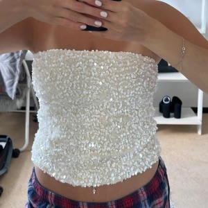 Vit paljett-tubtopp - Supersnygg vit tubtopp täckt av glittrande paljetter. Toppen är axelbandslös och har en rak bandeau-modell som sitter tight över överkroppen. Perfekt för dig som vill sticka ut och glänsa lite extra.