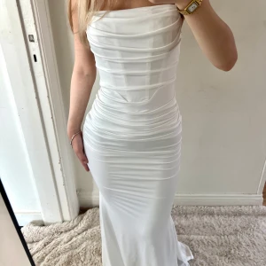 Vit långklänning med drapering - Supersnygg vit långklänning med figurnära passform och draperade detaljer över hela klänningen. Smala axelband design som ger en clean och elegant look. Perfekt för dig som vill sticka ut med en stilren och modern vibe. Aldrig använd, säljes pga av att den inte kommer till vidare användning. Ord pris: ca 300kr