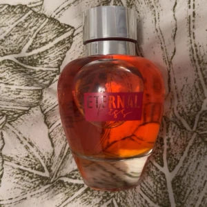 Eternal Kiss parfym 90ml La Rive - Eternal Kiss Eau de Parfum från La Rive, 90ml. Flaskan är rundad med en snygg röd-orange färg och har ett silverfärgat lock. Parfymen är tillverkad i Polen och har en modern, ungdomlig design som sticker ut i badrumshyllan. Helt oanvänd 