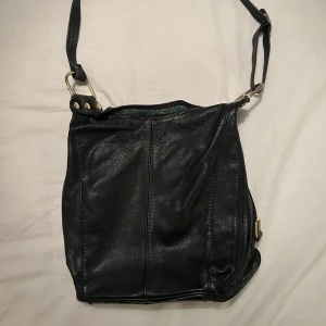 Svart axelväska  - Säljer en svart axelväska med justerbar rem och guldfärgade metalldetaljer. 