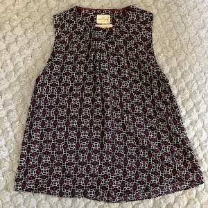 Mönstrad ärmlös topp Holly & Whyte - Snygg ärmlös topp från Holly & Whyte by Lindex med grafiskt mönster i vinrött, vitt och mörkblått. Toppen har rund halsringning med liten knappdetalj framtill och ett luftigt, rakt fall. Perfekt för dig som gillar färg och mönster!