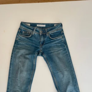Blå jeans från Pepe Jeans - Snygga blå raka jeans från Pepe Jeans med klassisk femficksdesign och ljusa slitningar. Modellen är Wiser Wash och har låg midja. Jeansen är i mjukt denimtyg och har detaljer som läderpatch bak och silverfärgade nitar.
