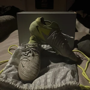 Nike phantom elite grått och lime - Snygga fotbollsskor från Nike i grått med limegröna detaljer och svart swoosh. Skorna har snörning, rund tå och ovandel i syntetmaterial för bra passform. Sulan är designad för grepp på planen och skon har en modern, sportig look. De är elite