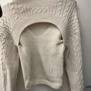 Beige stickad croppad tröja - Trendig beige stickad tröja med cool cut-out detalj över bröstet och kabelstickat mönster på ärmar och axlar. Tröjan har lång ärm och en croppad passform som ger en modern vibe. Perfekt för lager-på-lager och snygg till både jeans och kjol.