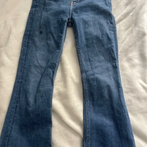 Blå bootcut jeans med klassisk look - Snygga blå jeans med bootcut-modell och klassisk femficksdesign. Jeansen har normal passform och är tillverkade i slitstarkt denimtyg med orangea sömmar. Perfekta för dig som gillar en tidlös och avslappnad stil.