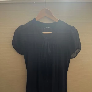 Mörkblå blus - Supersöt mörkblå blus från Orsay med korta ärmar och knytband vid halsen. Tunn och luftig känsla, perfekt för varmare dagar. Enkel och stilren design som är lätt att matcha med accessoarer