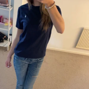 Marinblå t-shirt från Polo Ralph Lauren - Snygg marinblå t-shirt från Polo Ralph Lauren med klassisk vit logga broderad på bröstet. T-shirten har rund hals, korta ärmar och är gjord i mjuk bomull. Perfekt basic-plagg med stilren design och skön passform.