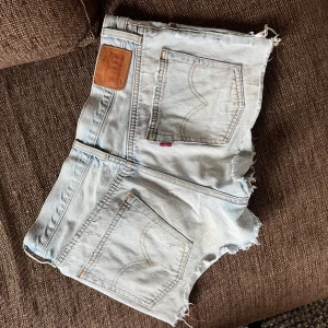 Levi's ljusblå jeansshorts med fransar - Snygga ljusblå jeansshorts från Levi's med råa, fransiga kanter och slitna detaljer. Klassisk femficksmodell med Levi's-lapp bak och röd etikett på bakfickan. Perfekta för en avslappnad och trendig look i sommar.