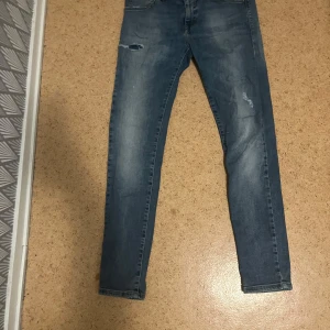 Blå slim jeans från SMOG 30/30 - Snygga blå skinny jeans från SMOG i storlek 30/30. Jeansen har slitna detaljer och en klassisk femficksdesign. De är tillverkade i stretchig denim för en bekväm passform och har en ljus tvätt med lätt slitning på benen.
