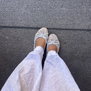 Vita spetsiga ballerinaskor med rosett - Säljer ett par vita ballerinaskor med spets och blommigt mönster. Skorna har rund tå och en söt rosett framtill. Skorna är använda en gång. Passar 38 o 37