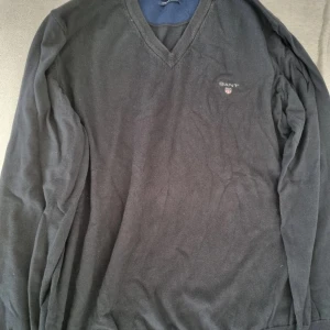 Svart v-ringad tröja från Gant -  v-ringad tröja från Gant i stretchig bomull. Klassisk design med broderad Gant-logga på bröstet och ribbade muddar. Perfekt för dig som gillar en stilren och enkel look. Passar lika bra till jeans som till chinos.