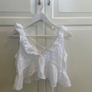 Vit volangtopp från Gina Tricot XS - Supersöt vit linnetopp från Gina Tricot i storlek XS. Toppen har volangdetaljer längs axelbanden och nederkanten, samt knytning i ryggen. Luftigt och lätt material som passar perfekt till varma dagar. Aldrig använd 