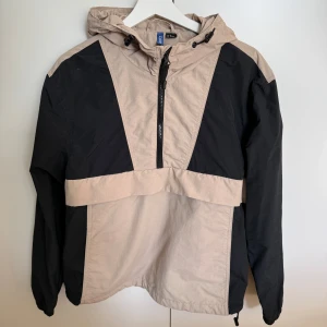Beige och svart vindjacka H&M Divided XS - 🌿Cool beige och svart anorakjacka med huva från H&M Divided.  🍒Jackan har en kort dragkedja framtill och en ficka med dragkedja på magen.  🌿Huva med snörning och half zip-dragkedja. 🍒Använd max. 2 gånger och tvättad. Som ny. 🌿Nypris över 400 kr. 🚭Djurfritt och rökfritt hem.