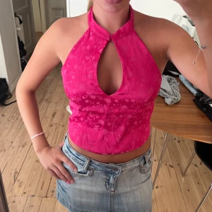 Rosa halterneck topp med blommönster - Säljer en snygg rosa halterneck topp med blommigt mönster och en cool cut-out framtill. Toppen är croppad och har en ärmlös design som knäpps i nacken. Perfekt för dig som vill sticka ut med en färgstark och trendig look!