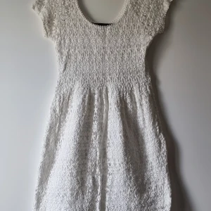 Vit spetsklänning från Zara Basic - Superfin vit kortklänning från Zara Basic med blommigt spetsmönster och rundad hals. Klänningen har korta ärmar och är fodrad under spetsen. Perfekt för sommarens alla tillfällen och ger en romantisk vibe.