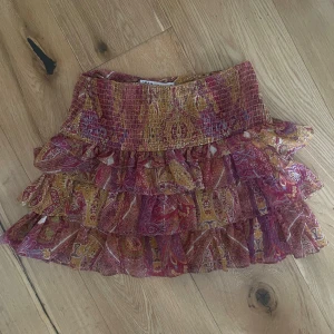 Mönstrad volangkjol från Zara - Eftertraktad och helt slutsåld kort mönstrad volangkjol från Zara i rosa, gult och rött. Kjolen har flera lager volanger och bred smock i midjan för en bekväm passform. 