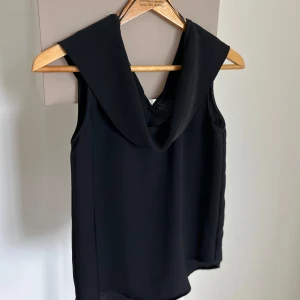 Svart ärmlös topp från Zara Basic - Stilren svart ärmlös topp från Zara Basic med bred krage. Toppen har en rak passform och är tillverkad i ett lätt, flowy material som känns skönt mot huden. Perfekt att styla med jeans eller kjol för en trendig outfit. Material: 100% polyester
