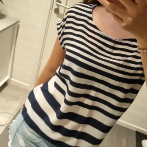 Randig topp från Stockh LM, marinblå/vit - Snygg topp från Stockh LM i storlek 36 med breda marinblå och vita ränder. Modellen är kortärmad med rund halsringning och har en liten metallring som detalj baktill. Tunt, lätt material som känns svalt och fräscht.