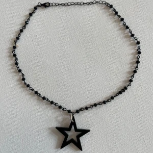 Svart halsband med stjärnhänge - Coolt svart halsband med små svarta pärlor och ett stort stjärnformat hänge i svart. Kedjan är tunn och smidig, perfekt för att ge din outfit en edgy vibe. Passar dig som gillar unika detaljer och vill sticka ut lite extra.