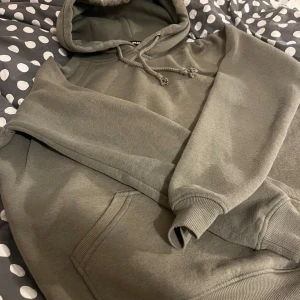 Grå hoodie från Bik Bok - Säljer en stilren grå hoodie från Bik Bok. Den har en klassisk design med en stor ficka framtill och justerbar huva med dragsko. Perfekt för en avslappnad look.
