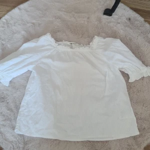 Vit blus från H&M - Säljer en söt vit blus från H&M med trekvartsärmar och volangdetaljer vid halsen. Perfekt för en somrig look. Blusen har en luftig passform och är tillverkad i ett lätt material.