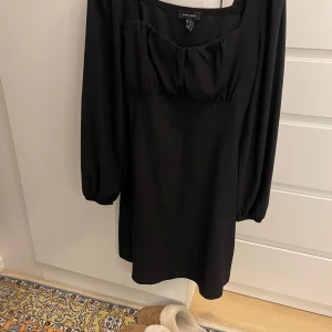 Svart klänning från New Look - Snygg svart klänning från New Look med långa ärmar och en elegant fyrkantig urringning. Klänningen har en stilren design med en subtil ribbad textur. Perfekt för en chic look!