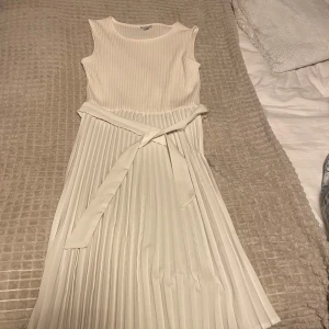 Vit ärmlös klänning från Guess - Säljer en elegant vit ärmlös klänning från Guess. Klänningen har en ribbad överdel och ett plisserat kjolparti med ett knytband i midjan. Perfekt för sommarens alla tillfällen! 🌼