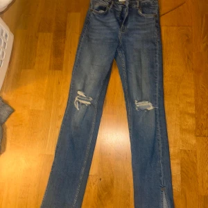 Blå jeansbyxor från Zara - Snygga blå jeansbyxor från Zara med slitna detaljer på knäna. De har en klassisk femficksdesign och en fin passform som ger en stilren look. Jeansen är från Zara och är använda typ 5 gånger. De har slits på sidorna.