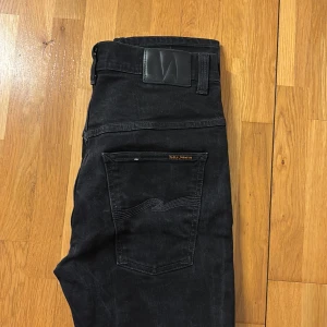 Svarta jeans från Nudie Jeans - Snygga svarta jeans från Nudie Jeans med klassisk femficksdesign. De har en diskret logga på bakfickan och en bekväm passform. Perfekta för en stilren look. Modell thin Finn. Storlek 34/32 men sitter som 32/32