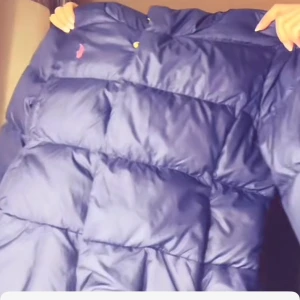 Blå dunjacka - Säljer en blå dunjacka med pufferdesign. Jackan har en hög krage och är perfekt för kyliga dagar. Den har en diskret logga på bröstet och stängs med dragkedja. Perfekt för att hålla värmen i stil! 💙