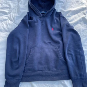 Blå hoodie från Ralph Lauren - Säljer en snygg blå hoodie från Ralph Lauren med det klassiska röda logotypbroderiet på bröstet. Tröjan har en stor ficka framtill och en bekväm huva. Perfekt för en avslappnad stil. Den är i toppen skick och passar xs. Skriv till mig om fler bilder eller frågor💛
