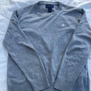 Grå tröja från Polo Ralph Lauren - Säljer en stilren grå tröja från Polo Ralph Lauren i mjuk pima bomull. Tröjan har en broderad logga på bröstet och långa ärmar med ribbade muddar. Perfekt för en avslappnad och klassisk look. Tröjan är i toppen kvalitet och inga skador vad jag vet skriv till mig vid frågor eller vid fler bilder💛