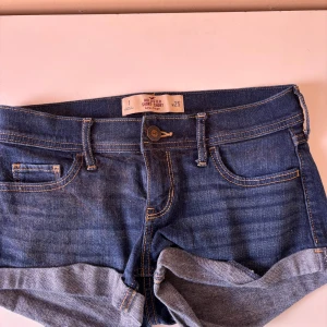 Blå jeansshorts - Snygga blå jeansshorts från Hollister med klassisk femficksdesign och uppvikta benslut. Perfekta för en avslappnad sommarlook. Midjan är låg och passformen är tight, vilket ger en smickrande siluett. Dom hata lite katthår på sig men tvättar dom såklart innan jag skickar.🥳