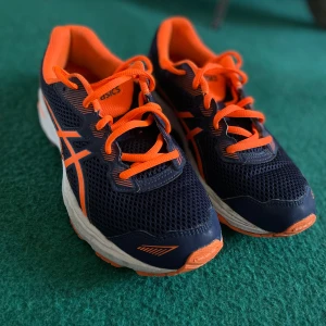 Blå och orange sneakers från Asics - Säljer ett par snygga Asics sneakers i blått och orange. Skorna har en sportig design med snörning och är tillverkade i syntetmaterial med gummisula. Perfekta för träning eller en aktiv vardag. Mycket fint skick, knappt använd skulle nog säga använda 1-2 gånger!
