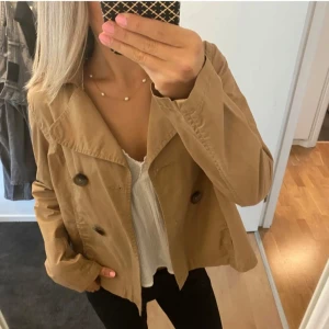 Beige trenchcoat med knappar - Snygg beige trenchcoat med stora knappar framtill. Perfekt för våren, med en klassisk krage och normal passform. En stilren jacka som funkar till många olika outfits!😍 unik & trendig, säljs inte längre😚passar 34/36