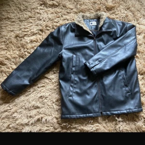 Svart jacka i skinnimitation  - Svart jacka i skinnimitation, i fint skick förutom små slitningar längst ut på armarna
