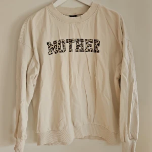 Beige sweatshirt med leopardmönster - Säljer en beige sweatshirt med texten 'MOTHER' i leopardmönster på bröstet. Tröjan har långa ärmar och ribbade muddar vid ärmslut och nederkant. Perfekt för en avslappnad stil. Har en fläck baktill.
