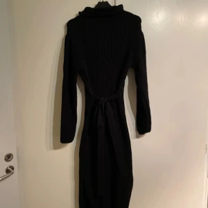 Svart ribbad klänning från Shein - Snygg svart ribbad klänning från Shein med långa ärmar och knytband i midjan. Perfekt för en stilren look. Tillverkad i 100% polyester.