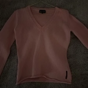 Rosa stickad tröja  - Säljer en stilren rosa stickad tröja från Jean Paul. Tröjan har en v-ringad design och långa ärmar, perfekt för kyligare dagar. Den är mjuk och bekväm, idealisk för både vardag och avslappnade tillfällen.