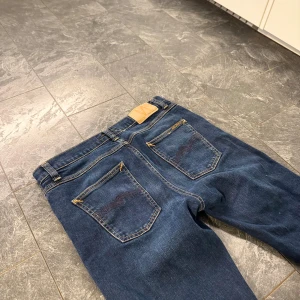 Nudie Jeans med slitningar - Snygga blå jeans med slitningar på framsidan. De har en klassisk femficksdesign och en knappgylf. Perfekta för en avslappnad stil.