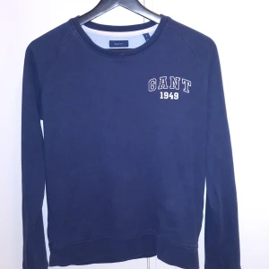Mörkblå tröja från Gant - Säljer en stilren mörkblå tröja från Gant med tryck 'GANT 1949' på bröstet. Tröjan har långa ärmar och en rund halsringning. Perfekt för en avslappnad stil.