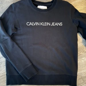 Svart sweatshirt från Calvin Klein Jeans - Säljer en stilren svart sweatshirt från Calvin Klein Jeans med deras logga tryckt i vitt på bröstet. Tröjan har långa ärmar och en rund halsringning. Perfekt för en avslappnad look. Svart fin färg, svår att fota.