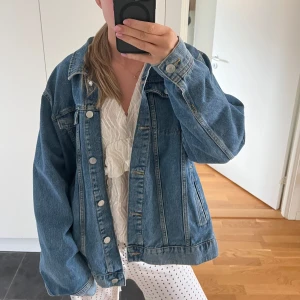 Blå jeansjacka från Lindex - Säljer en klassisk blå jeansjacka från Lindex i storlek XL men passar på mig som är en storlek s/m för en lite oversized look. Jackan har en normal passform med långa ärmar och knappar framtill. Perfekt för vår och sommar! 