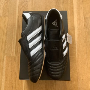 Svarta adidas taekwondo sneakers - Snygga svarta Adidas taekwondo skor med klassiska vita ränder och en minimalistisk japansk-inspirerad design.   