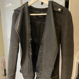Svart skinnjacka från Vero Moda - Snygg svart skinnjacka från Vero Moda med dragkedja och stilrena detaljer. Jackan har en klassisk bikerstil med långa ärmar och en cool look. Perfekt för att ge din outfit en edgy touch. Storleken är dock missvisande, den faller definitivt myclet mindre, stor S skulle jag säga. 