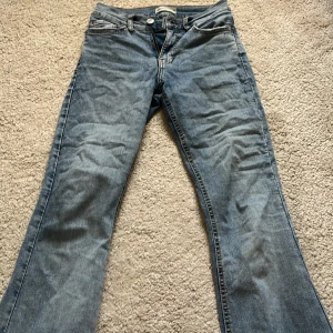 Blå jeans med bootcut från Gina tricot  - Säljer ett par klassiska blå jeans från Gina tricot med bootcut-stil. De har en knapp och dragkedja framtill samt två bakfickor. Perfekta för en avslappnad look.