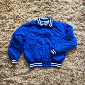 Blå bomberjacka med tryck - Säljer en blå bomberjacka med vitt tryck på ryggen. I fint skick