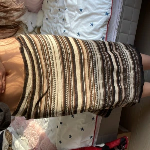 Randig kjol - Snygg randig kjol från Laura Clement i jordnära toner som brunt, beige och svart. Kjolen har ett dekorativt bälte i midjan och är perfekt för en stilren look. Tillverkad i Turkiet.